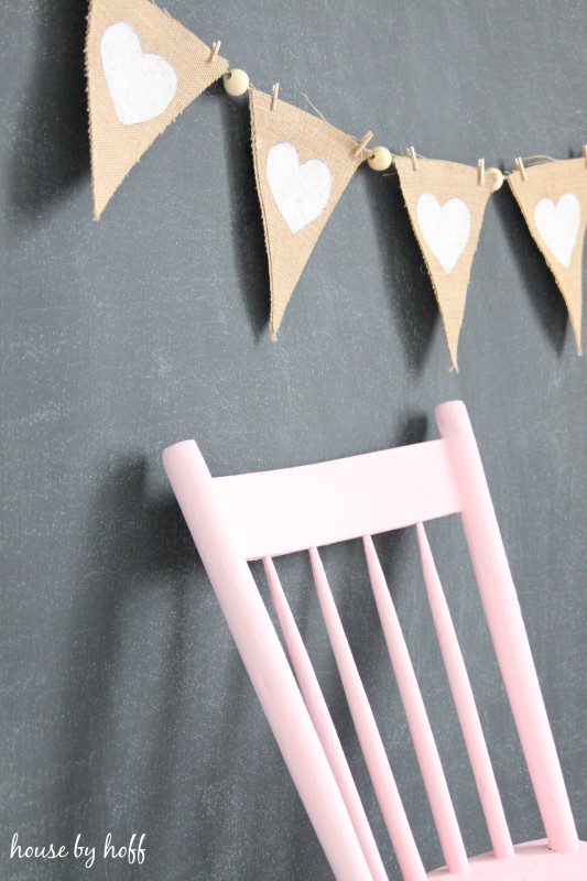 A chalkboard wall with a pink chair leaning against it and the Valentines pennant strung across the chalkboard.