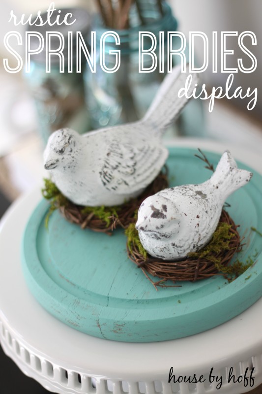 Two little white decorative birds on faux nests on a cake stand.