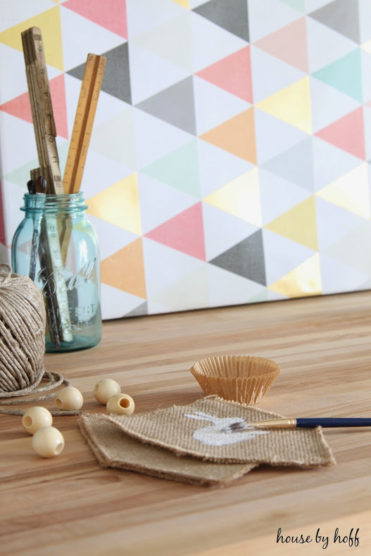 A paint brush, with white paint on it, a clear blue mason jar with rulers in it on the diy piping table.