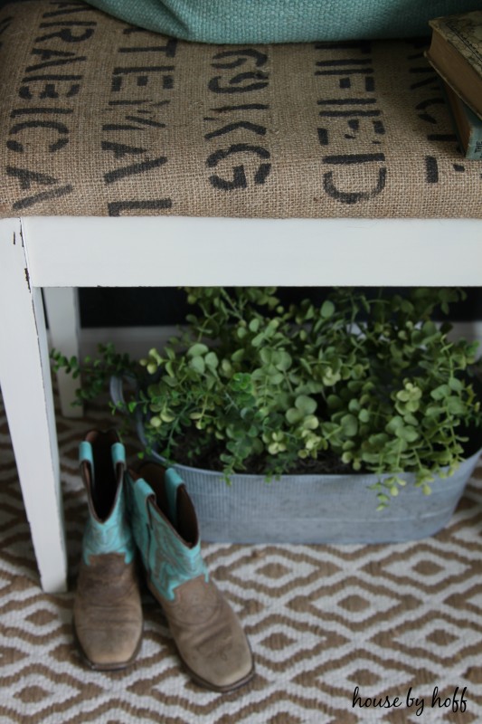 The piano seat with cowboy boots and a plant under it.