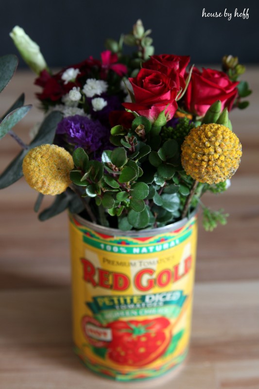 A tomato tin can filled with red, yellow and purple flowers.