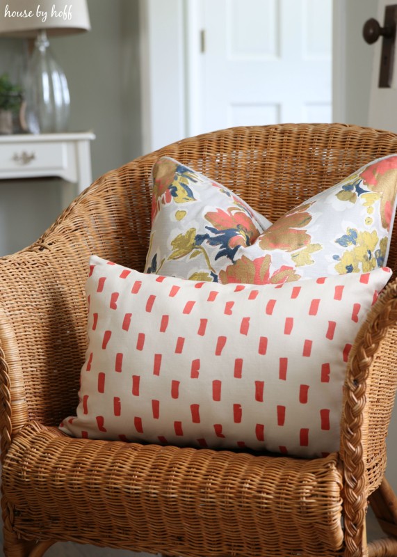 Red and white throw pillow and a flower pillow on a wicker chair.