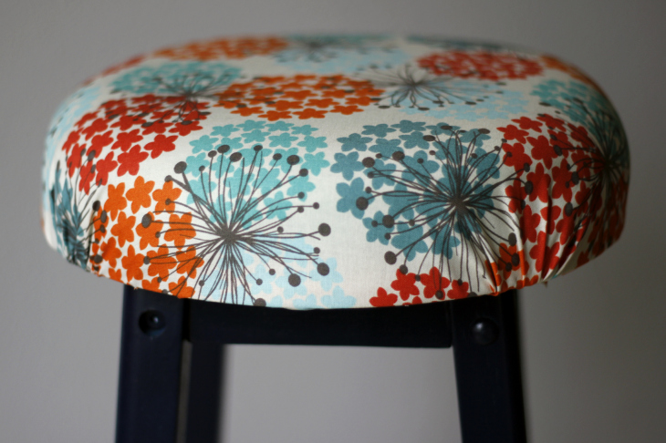 Blue, orange, red, floral fabric on top of black stool.