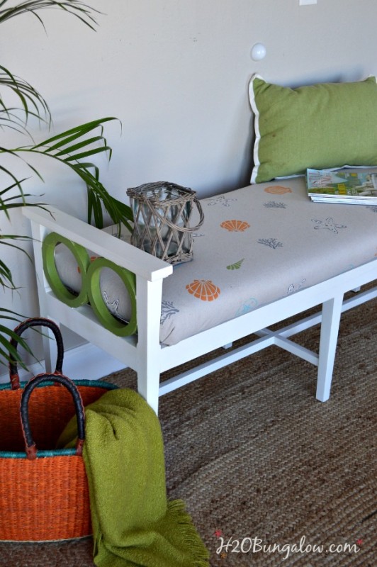 Outdoor bench with a green and white and seashell cushion.