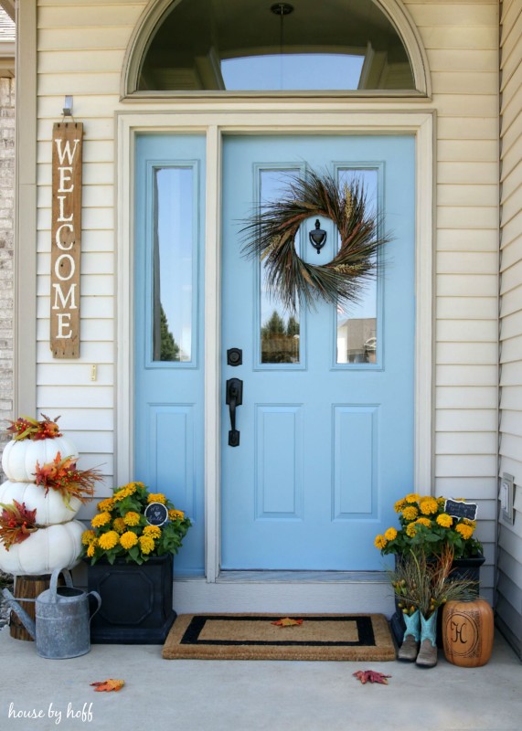 Front porch with wreath on door and white pumpkins stacked in front.