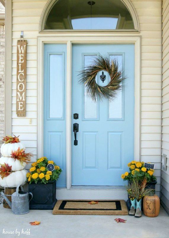 Light blue front door with fall wreath and yellow flowers in planters.