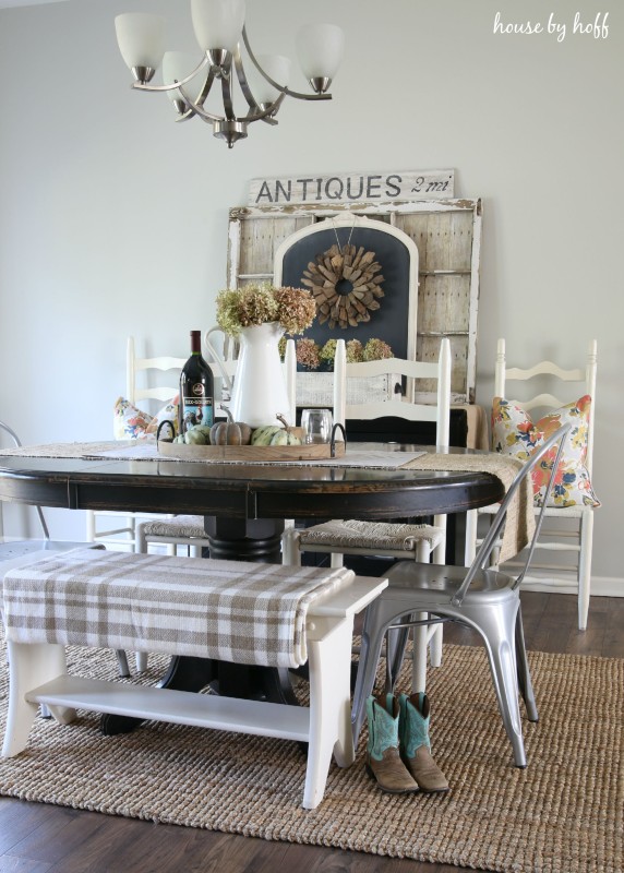 Dining room table with cowboy boots beside it, and a wooden bench by the table with a checkered blanket on it.