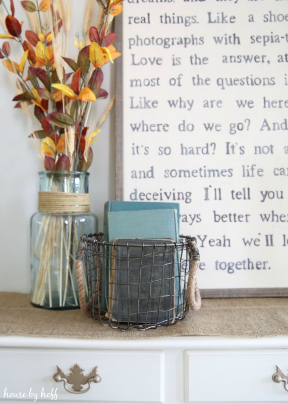Lyrics, vase filled with leaves, and a metal container with antique books in it on the side table.