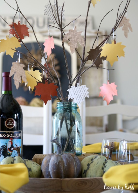 Multi colored paper leaves hanging on branches in a clear vase.