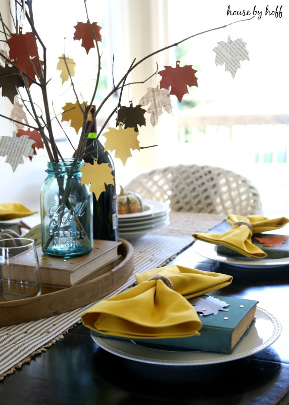 The paper leaf tree, plates with yellow cloth napkins and antique books on the plates.