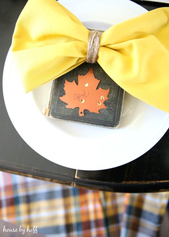Antique book with a maple leaf cutout on it and a yellow napkin.