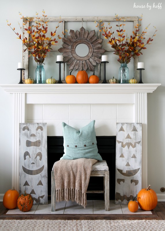 Firplace mantel with pumpkins in front and autumn leaves in light blue glass vase.