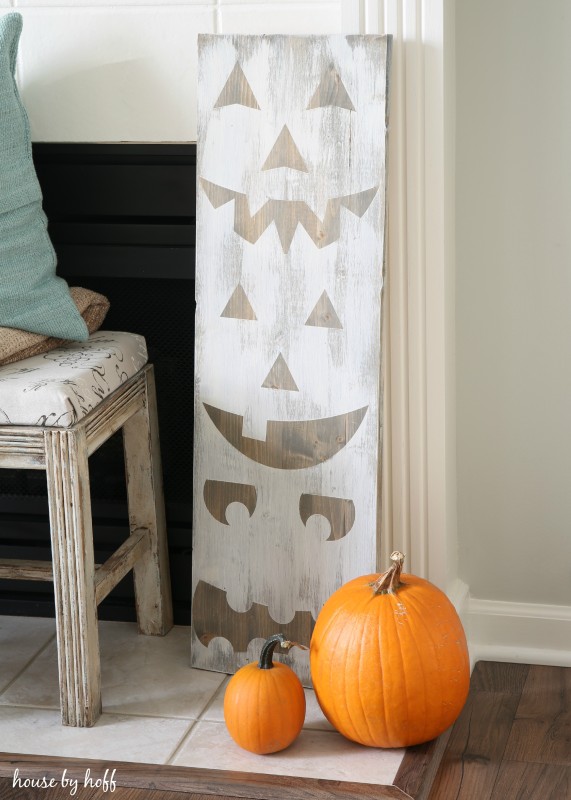 The DIY pumpkin signs leaning agains the fireplace with a large and small pumpkin in front of it.