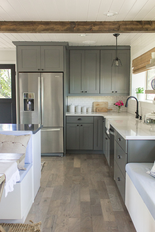 Gray kitchen cabinets with a wood beam and white counters.