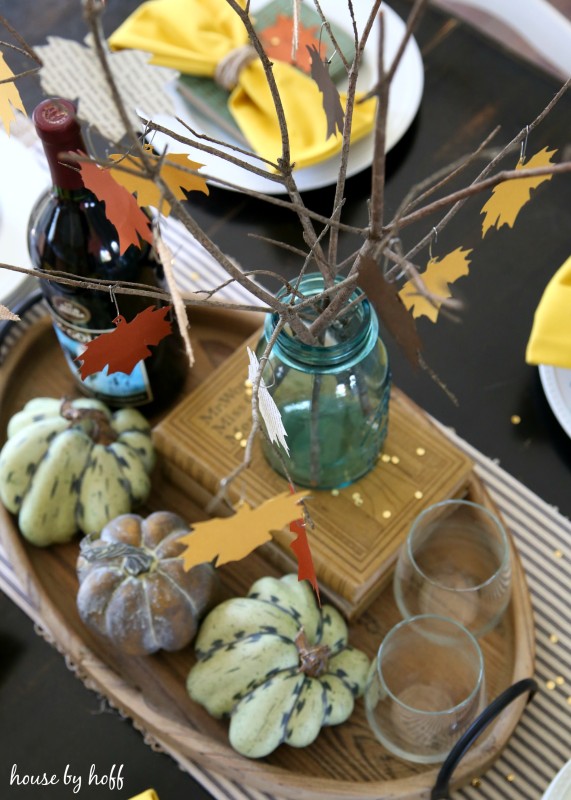 The leaf centerpiece plus mini pumpkins beside it and a bottle of wine.