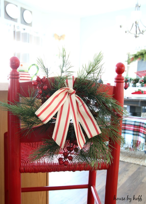 Holiday bar stool painted red, with a sprig of evergreen, red berries and a bow.