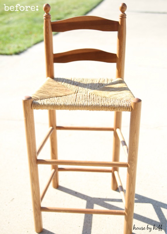 A wooden and wicker bar stool outside by the grass.