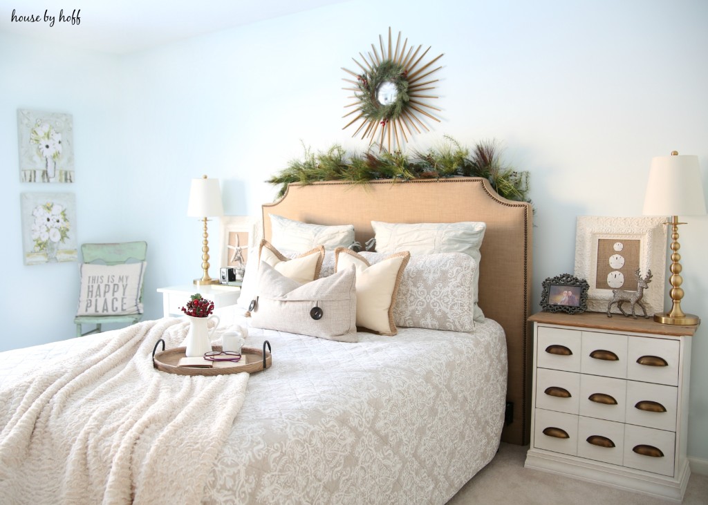 Neutral bed and pillows with a green wreath above the bed.