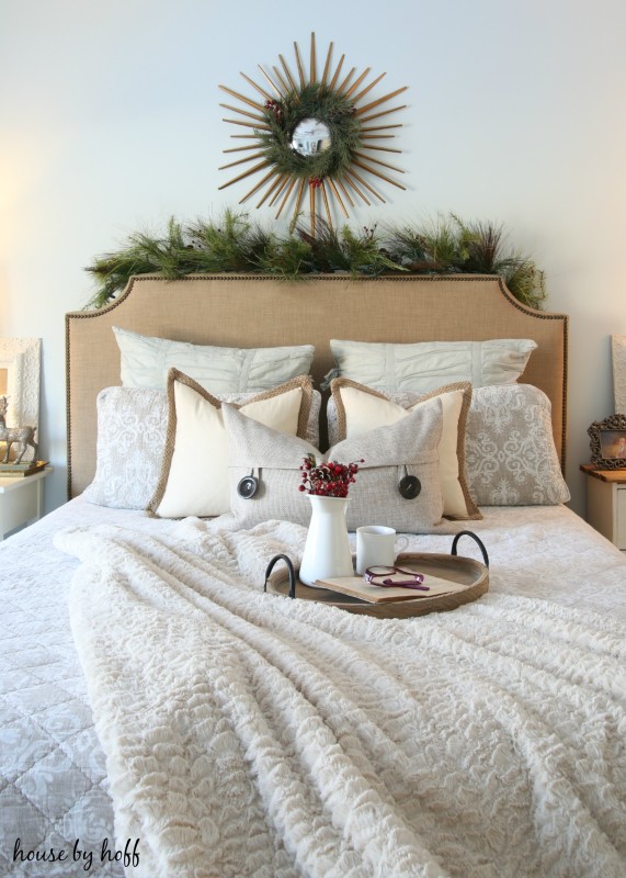 A tray on the bed with red berries in the vase and a cup of tea.