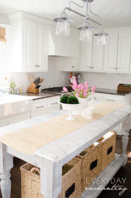 A marble kitchen island with pink tulips on it and white kitchen cabinets.