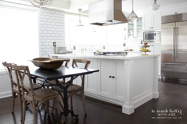 A white kitchen island with subway tile and a small table in the dining area.