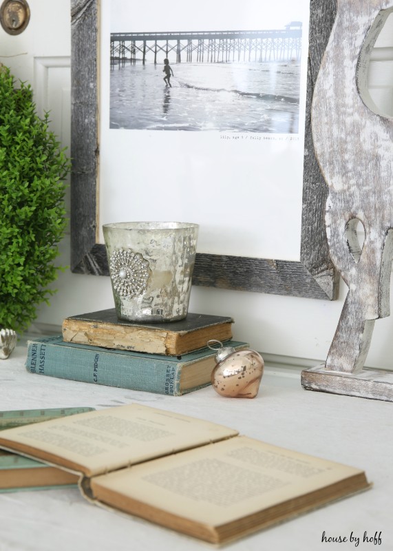 Wooden framed picture on wall of a little girl on the beach, and a candle on antique books on the desk.