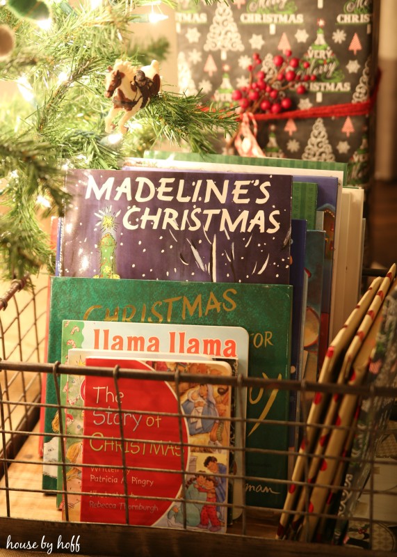 Christmas books in a wire basket are underneath the Christmas tree.