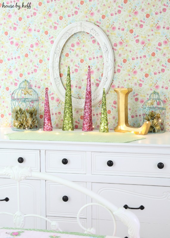 A white dresser with black knobs and sparkly Christmas trees mini on top.