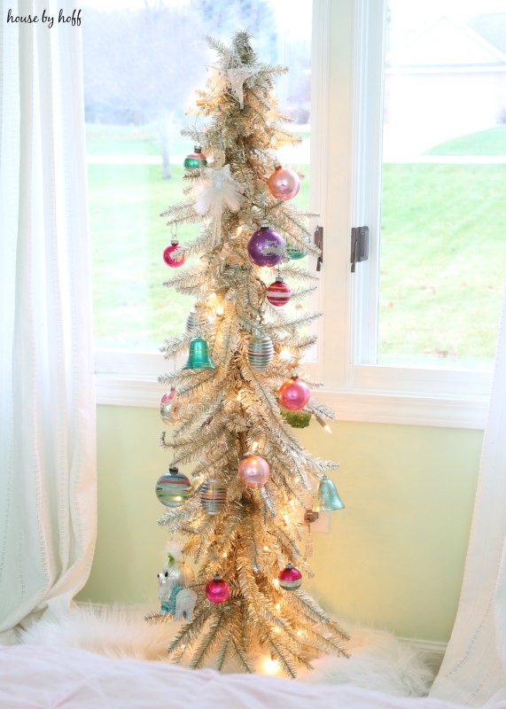 A champagne vintage Christmas tree in front of a window in bedroom.