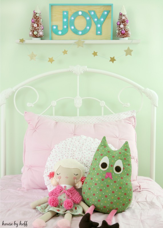 A white bed frame with pink blankets and Joy in a wooden picture frame above the bed.