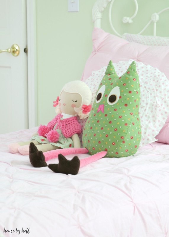 A doll and stuffed animal on the pink bed.