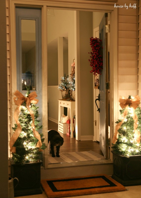 The door opened to the house with lit mini trees flanking the door outside.