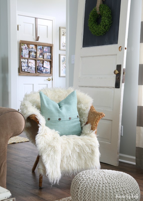 A small wicker chair with faux white fur and a blue pillow on it.