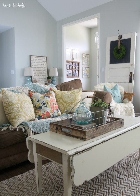 A living room couch with pillows on the couch in floral pattern, and a white coffee table in  the middle of the living room.