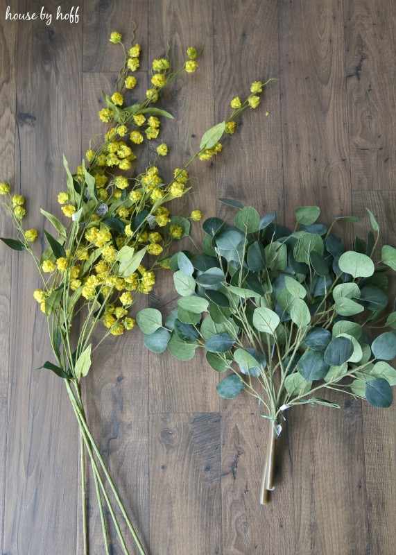 The bundle of yellow flowers and a bundle of eucalyptus on the table.