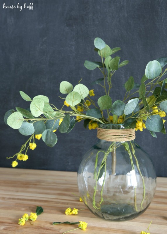 The eucalyptus and yellow flowers in the vase on the table.