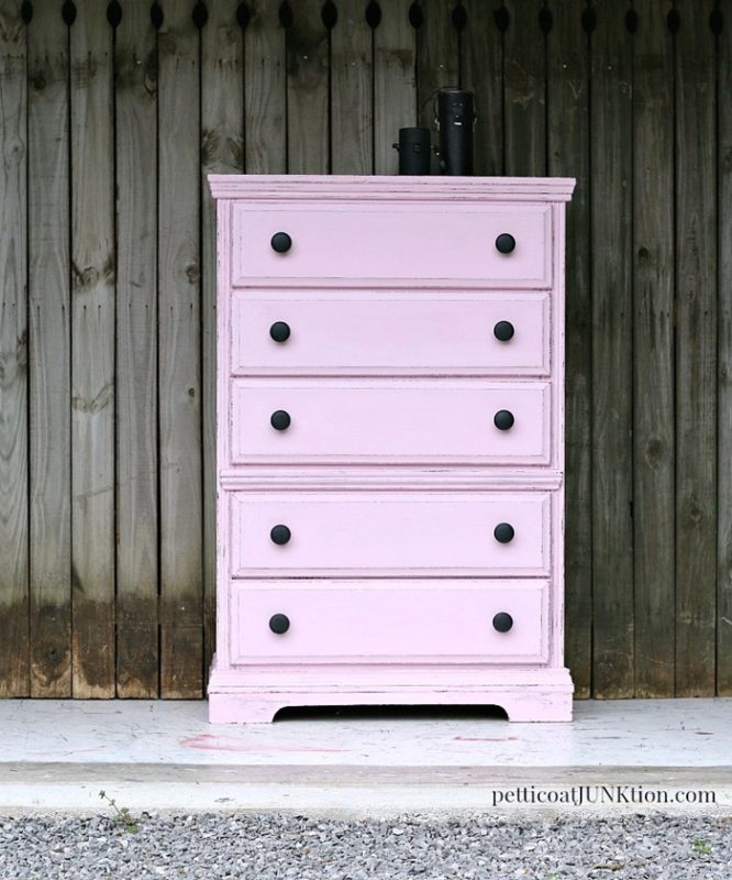 A soft pink dresser with black knobs.