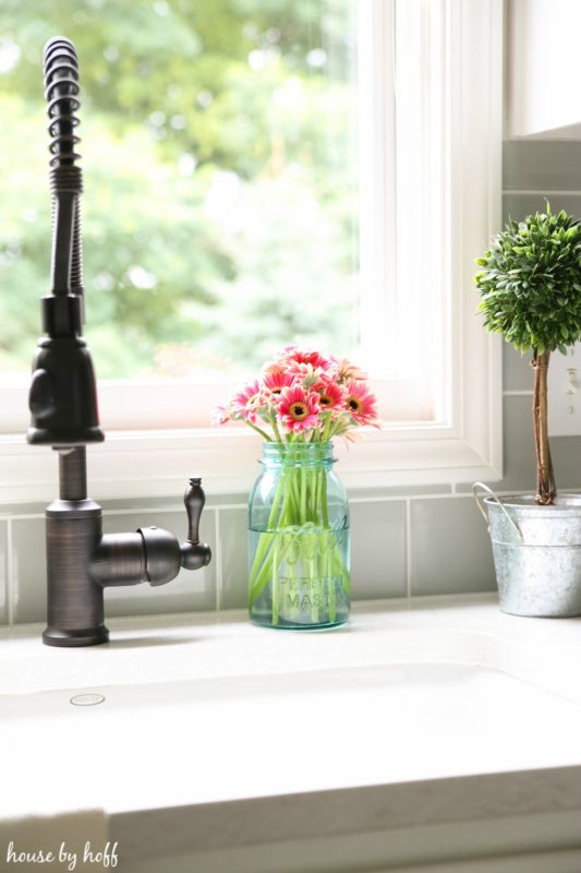 Pink flowers in glass jar beside faucet.