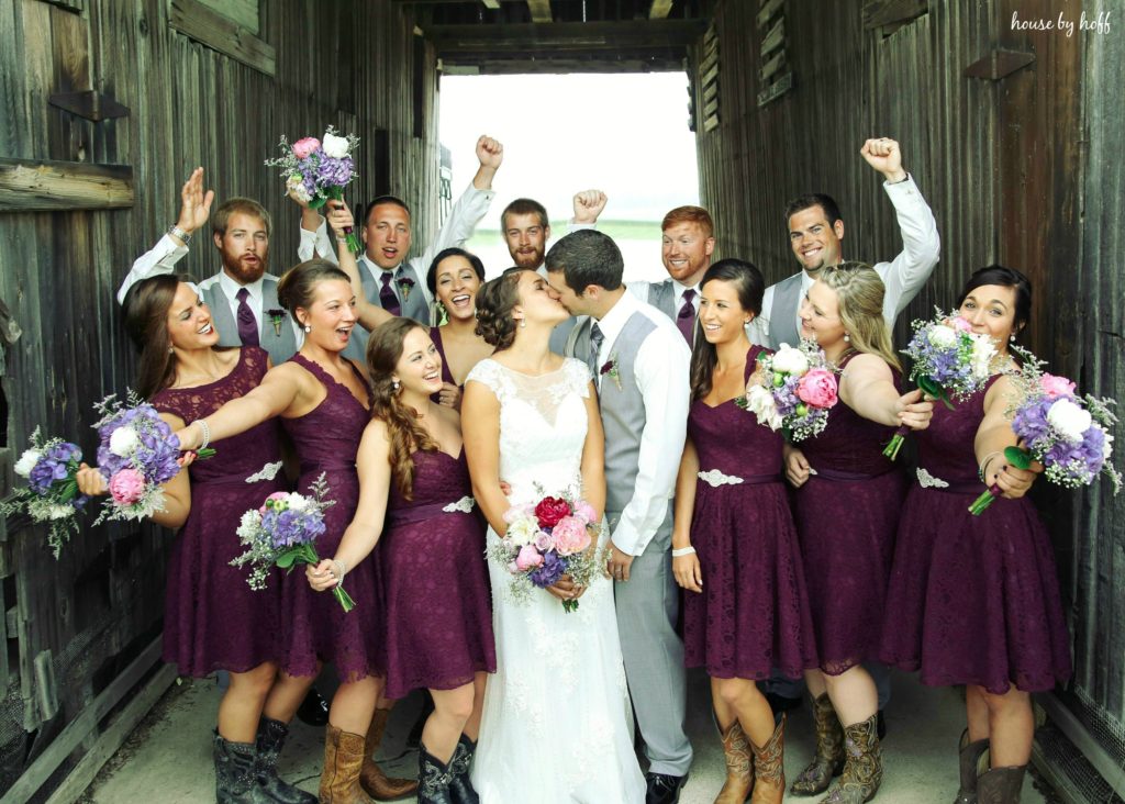 The bride and groom kissing with their wedding party around them.