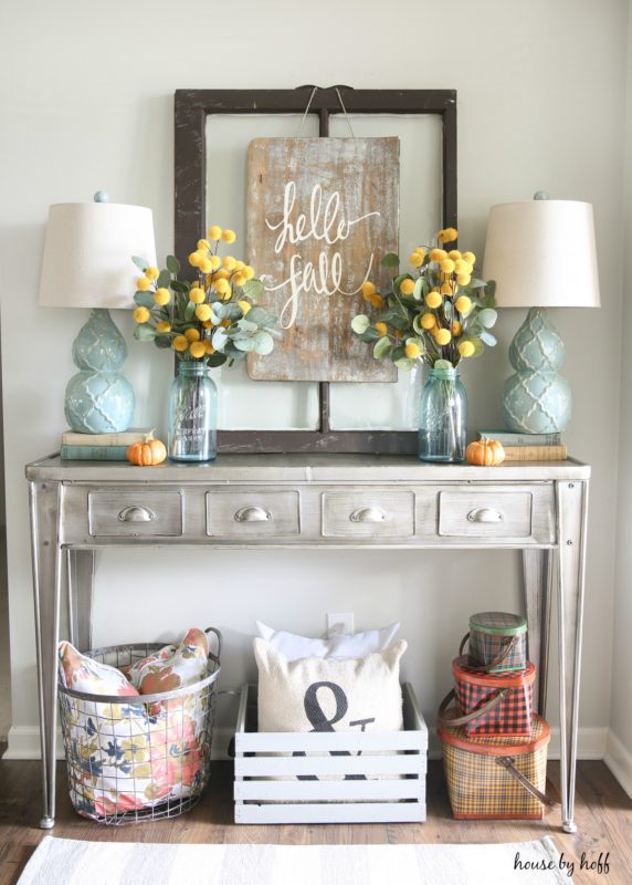 Side table with drawers, yellow flowers in vases on table and a Hello Fall sign hanging above it.