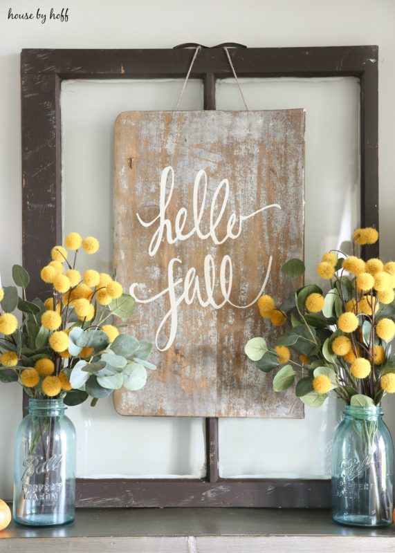 Yellow flowers in clear blue glass jars in front of diy fall sign.