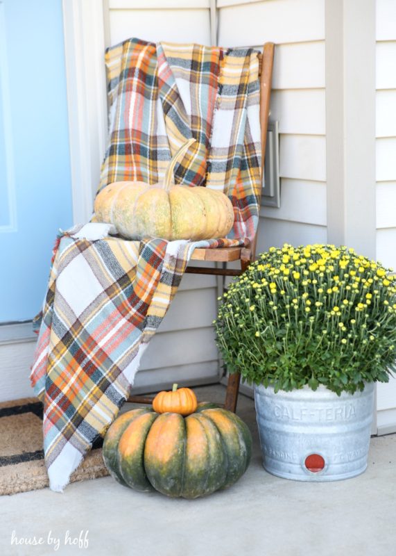 Plaid blanket on chair with a pumpkin on it and a galvanized bucket filled with yellow flowers.