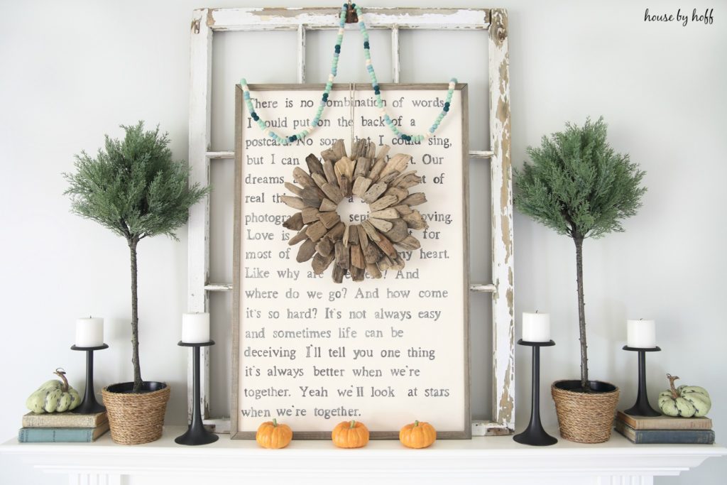 Wooden sign above the fireplace with topiary trees, candles and pumpkins on mantel.