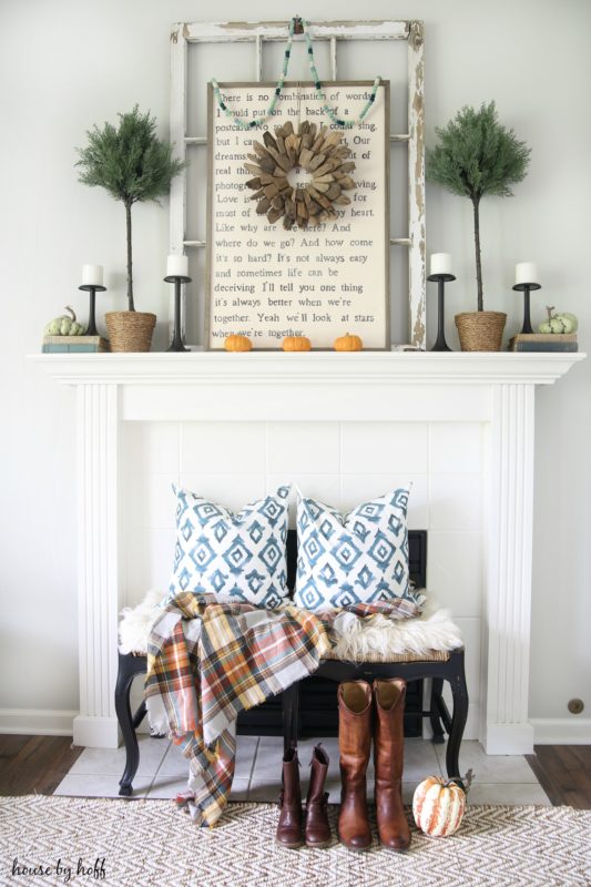 White fireplace with bench in front of it and pillows on bench, cowboy boots in front, and candles on the mantel.