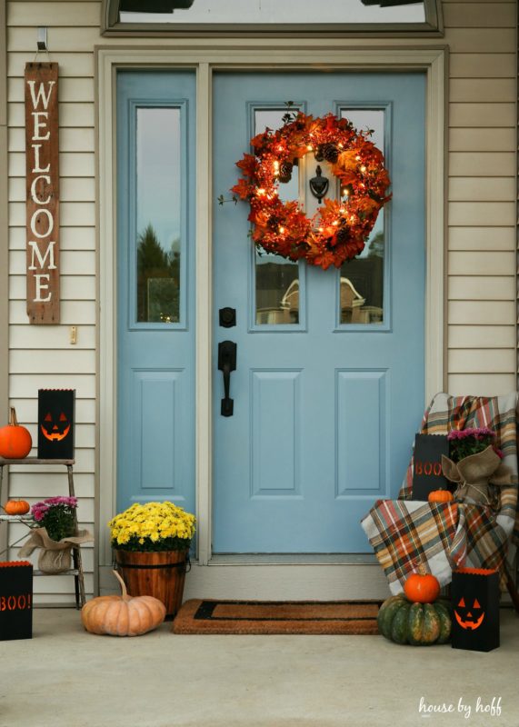 Halloween wreath lit up on door, with pumpkins on the front porch.