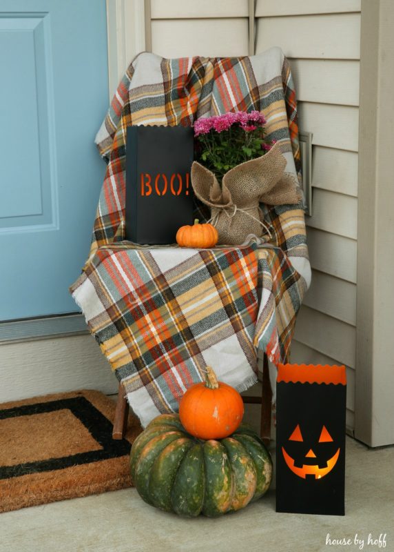 Halloween boo bag and pumpkins around chair on front stoop.