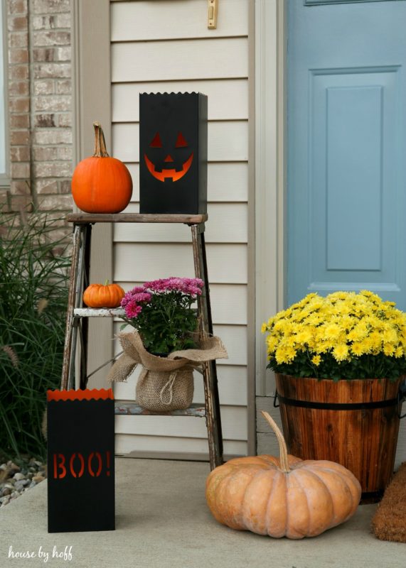 Small stepladder on front porch with pumpkins on it and scary pumpkin faces.