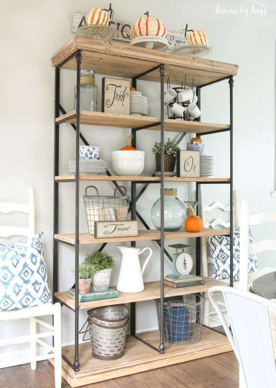 Metal and wood shelf behind dining table with mini orange pumpkins on them.