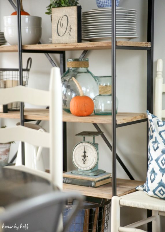 Glass jars, a scale and plates on shelving unit in dining room.