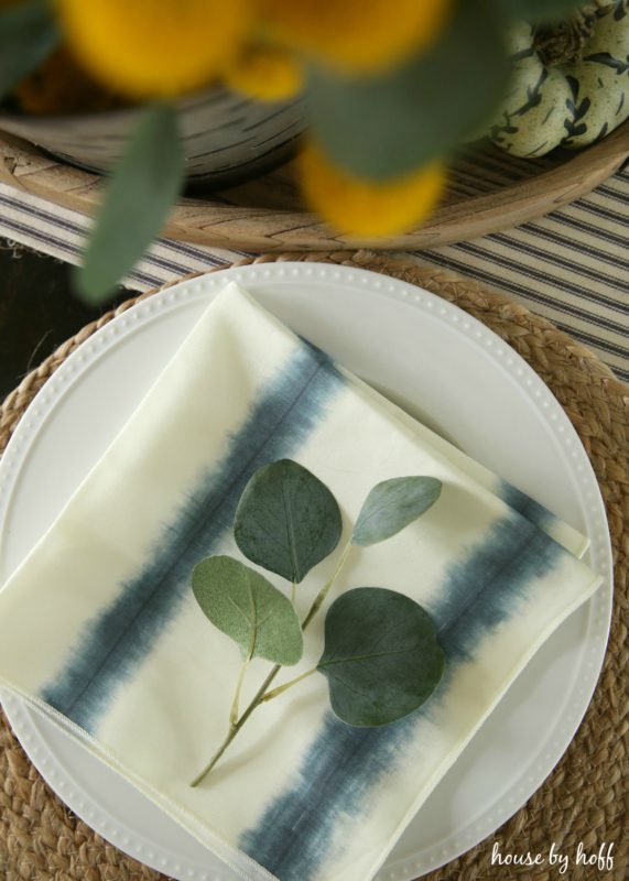 White plate with tie dyed napkin blue and white and eucalyptus leaf on it.